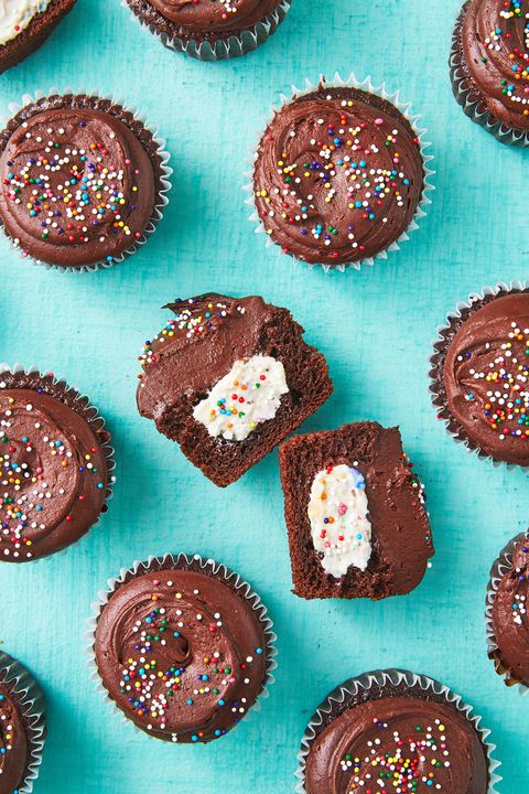 cheesecake stuffed chocolate cupcakes with chocolate frosting and rainbow nonpareil sprinkles on a teal background