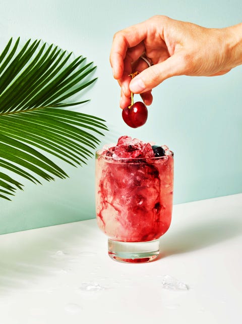 a cherry simple syrup cocktail with someone topping it off with a cherry