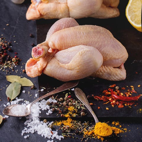 Two Raw mini Chicken with sea salt and different spices over black slate board