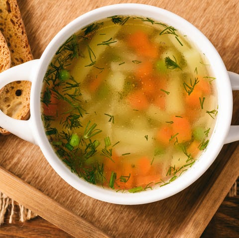 Chicken soup in white bowl on wooden tray.