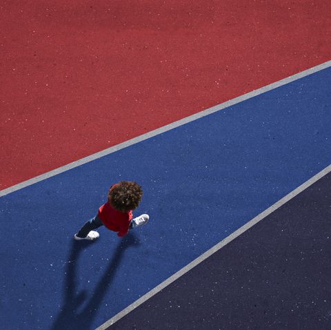 child dressed in red, walking across red and blue painted asphalt