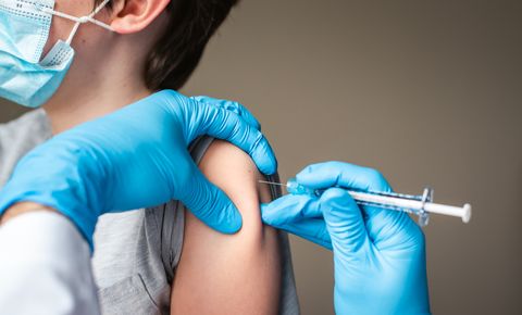 child wearing mask getting vaccinated by doctor holding a needle
