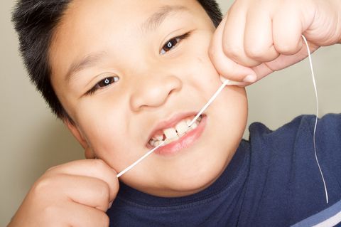 Niño que trabaja para usar hilo dental en sus dientes frontales