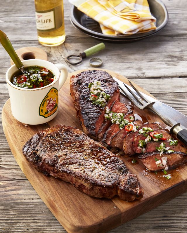 two steaks on a cutting board with chimichurri sauce spread on one