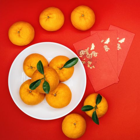 jeruk keprok utuh di piring putih dengan latar belakang merah