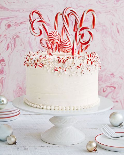 layer cake covered in white frosting with crushed peppermints pressed around the top edges and various sized and shaped candy canes sticking out of the top