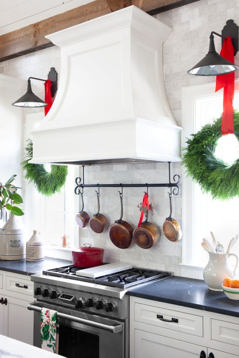 a marble backsplash and white hood range cover with copper pots hanging on a rack underneath and a holiday wreath on each side