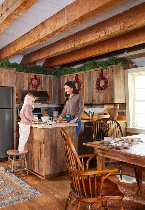 a mom and daughter decorate cookies at an island in a rustic kitchen with wood cabinets and rough hewn beams