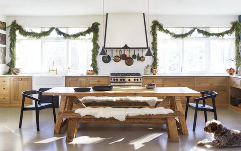 swaths of fresh greenery frame the windows in a simple kitchen with the wood lower cabinets and a long farmhouse table