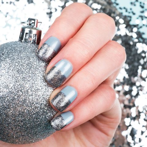 woman hand with baubles and festive glitter manicure on blue shiny background christmas holiday concept