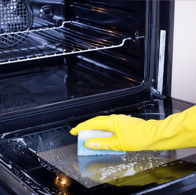 close up of female hand with yellow protective gloves cleaning oven door