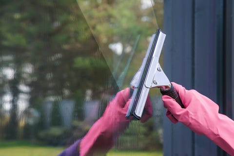hand in pink rubber protective glove washing and cleaning window with professionally squeegee early spring windows cleaning on the trees background