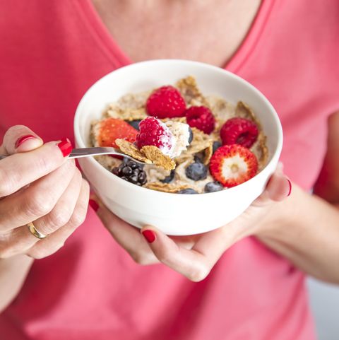 close up crop of woman holding a bowl containing homemade granola or muesli with oat flakes, corn flakes, dried fruits with fresh berries healthy breakfast