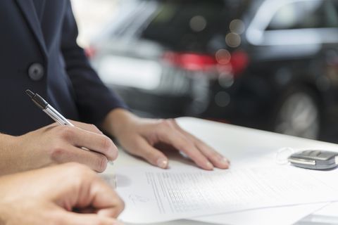 Close up customer signing financial contract paperwork in car dealership
