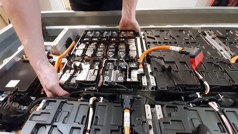 close up of a mechanics hands disassembling an electric car battery on top of a trailer inside a mechanic shop