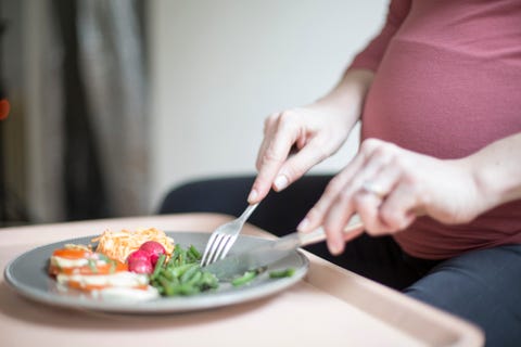 Close up of a pregnant woman eating a plate of salad and vegetable.