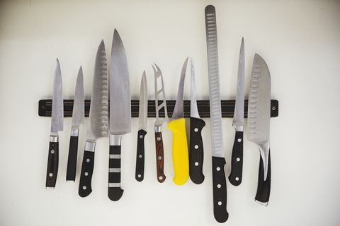 Close up of a selection of knives on a magnetic strip in a kitchen.