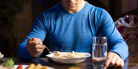 Man eet na training een bord paste en sla en drinkt een glas water aan tafel.