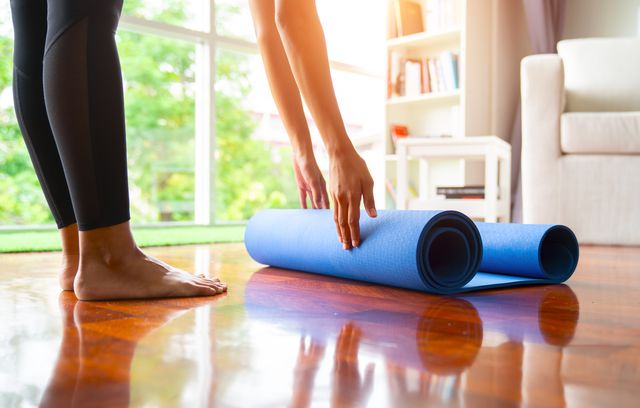 close up of attractive young woman folding blue yoga or fitness mat after working out at home in living room