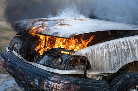 Cerca del motor del coche en llamas después de una colisión frontal en el borde de la carretera con llamas y humo