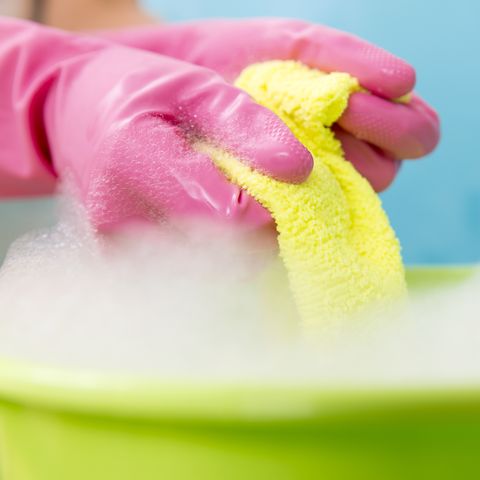 Close-up of cleaner woman hand squeezing cloth in bucket filled with soap
