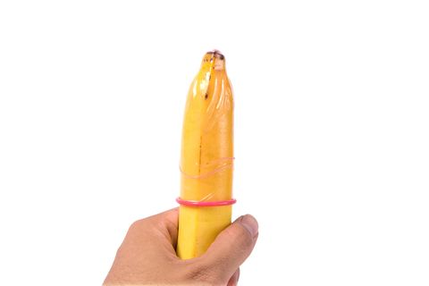 Close-Up Of Condom On Banana Being Held By Man Against White Background