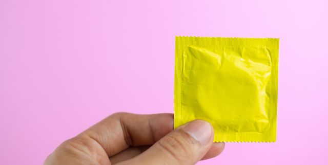 close up of cropped hand holding condom packet against pink background