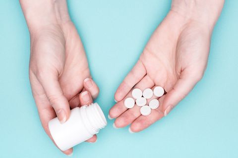 Close-up of female hands with medication bottle and white pills over pastel blue background patient taking medication