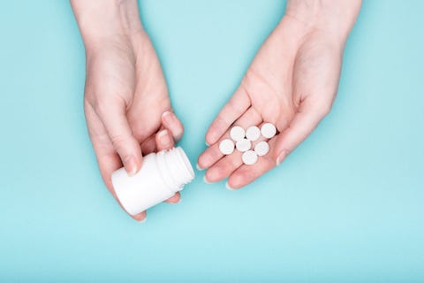 Close-up of female hands with medication bottle and white pills over pastel blue background patient taking medication