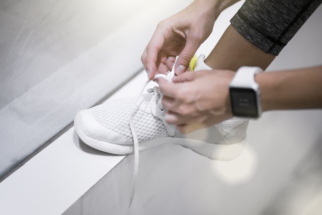 close up of female hands tying sneakers with smartwatch
