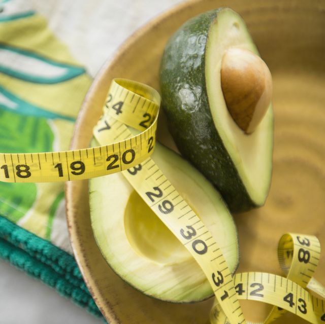 close up of halved avocado, measuring tape and napkin on plate