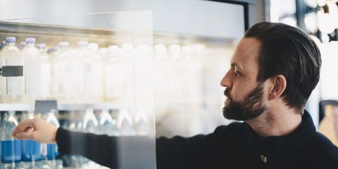 Close-up of man buying water bottle from glass cabinet at store