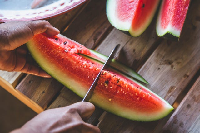 close up of man cutting watermelon slices on table