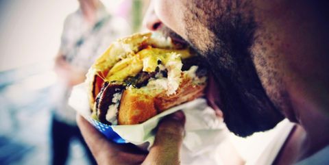Close-Up Of Man Eating Cheeseburger On Street