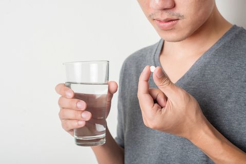 Close-Up Of Man Taking Pill Against White Background