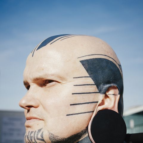 close-up de um homem com tatuagens e tampão de ouvido contra o céu