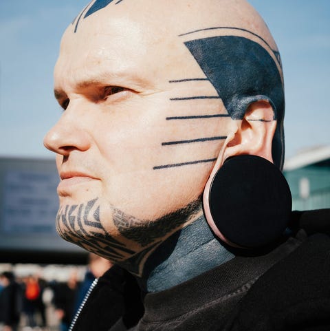 close-up de um homem com tatuagens e tampão de ouvido contra o céu