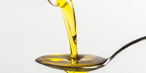 Close-Up Of Olive Oil Pouring On Spoon From Container Against White Background