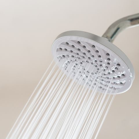 close up of shower head spraying water against white wall