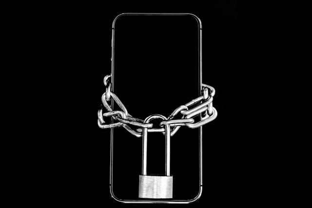 closeup of smart phone with padlock and chain over black background