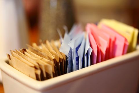 close up of sugar and sweetener packets in container at cafe