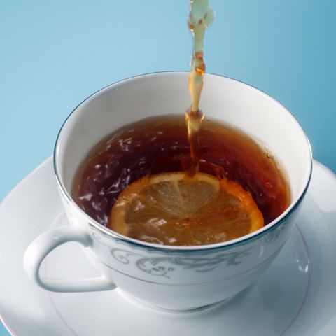 Close-Up Of Tea Being Poured In Cup Over Blue Background