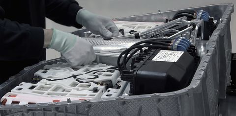 Near the hands of a worker adjusting several cables for the lithium battery of electric cars on the indoor table of an electric car factory