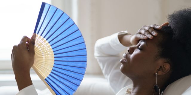 close up of tired woman holding hand fan at home