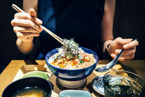 Close up of woman enjoying freshly served traditional Japanese seafood donburi with chopsticks in a restaurant