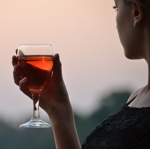 close up of woman holding wineglass against sky during sunset