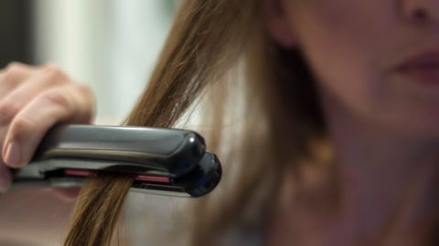 close up of woman straightening hair at home