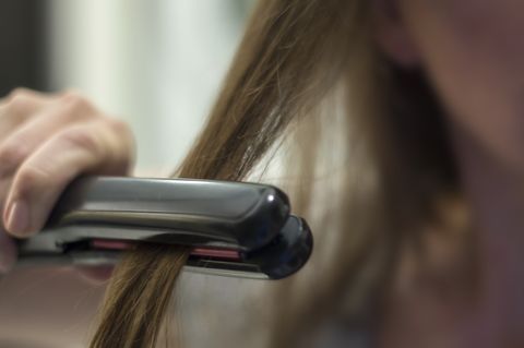 close up of woman straightening hair at home