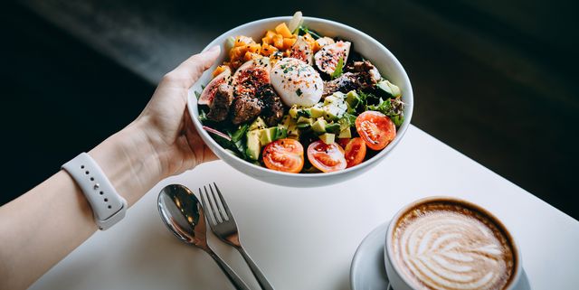 close up of woman's hand holding a bowl of fresh beef cobb salad, serving on the dining table ready to enjoy her healthy and nutritious lunch with coffee maintaining a healthy and well balanced diet healthy eating lifestyle