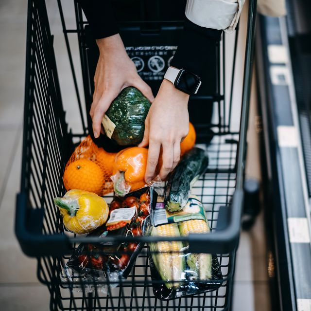 close up of woman's hand shopping for fresh groceries in supermarket and putting a variety of organic vegetables in shopping cart